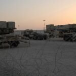 Two Patriot PAC-3 missile launchers positioned at a military air base.