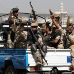 Armed Houthi fighters carrying rifles and an RPG launcher in the back of a pickup truck in Yemen.