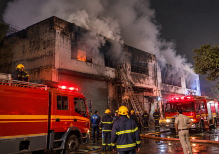 Fire engines and firefighters responding to a nighttime fire at an industrial building.