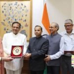 Prime Minister Narendra Modi stands with government officials holding a commemorative plaque in front of Indian national flags.