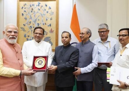 Prime Minister Narendra Modi stands with government officials holding a commemorative plaque in front of Indian national flags.